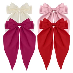 Detail of four oversized satin bow hair clips in cream, pink, rose, and red colors