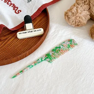 Détail d'un peigne à cheveux en acétate fleuri vert et orange sur bois naturel