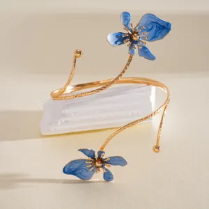 Gedetailleerde weergave van een gouden armband met twee blauwe emaille bloemen