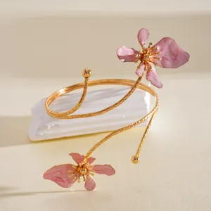 Detailweergave van een goudkleurige bovenarmband met elegante roze emaille bloemen.