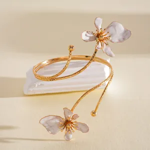 Gedetailleerd overzicht van een goudkleurige armband met witte geëmailleerde bloemen.