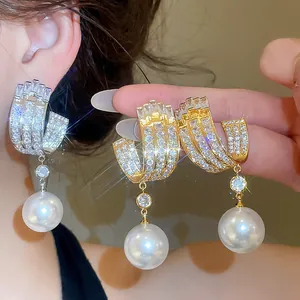 Dettaglio di orecchini di lusso in zircone oro e argento con grandi perle pendenti