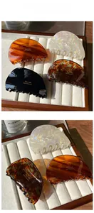 Détails de quatre pinces à cheveux en acétate aux finitions marbrées et ambrées dans leur coffret