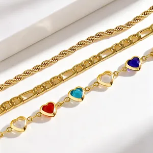 Close-up of layered gold anklet set featuring Figaro chain and colorful heart charms.