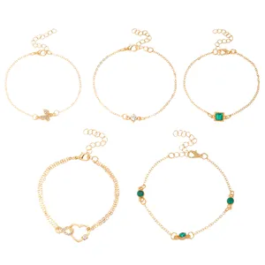 Set of five gold bohemian adjustable anklets with various charms and green crystals.