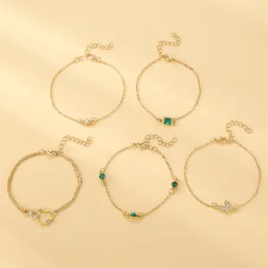Detail of five adjustable gold bohemian anklets with butterfly heart and emerald charms