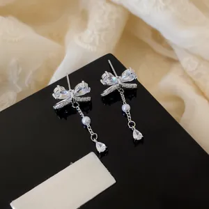 Close-up detail of elegant silver bow earrings with sparkling zircon and pearl drop