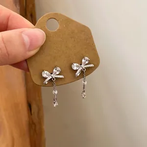 Detailed close-up of elegant zircon bowknot tassel earrings with pearl drops on card.