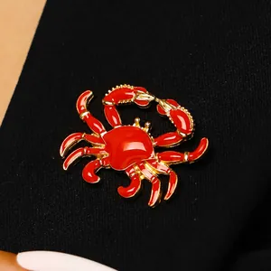 Detailansicht einer lebhaften roten Emaille-Krabbenbrosche mit goldfarbenen Kanten.