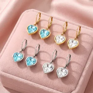 Elegante herzförmige Kristallohrringe in Gold und Silber auf einer rosa Schmuckschatulle
