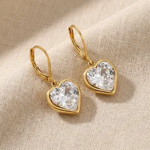 Nahaufnahme von eleganten goldenen Herzohrringen mit weißen Kristallen auf Stoff