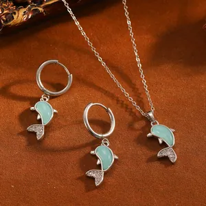 Detailansicht eines silbernen Delphin-Schmucksets mit grüner Emaille und glitzernden Strasssteinen