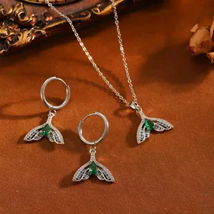 Detailaufnahme von Delfinschwanz-Schmuckset mit grünen Steinen auf braunem Sand.