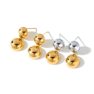 Dettaglio di orecchini pendenti minimalisti in acciaio con due sfere oro e argento.