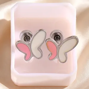 Dettaglio di orecchini ad ala d'angelo con smalto rosa e bianco su sfondo di raso beige