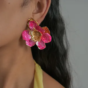 Gros plan d'une grande boucle d'oreille fleur en émail rose avec des bords dorés sur un modèle