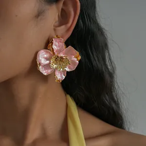 Gros plan d'une boucle d'oreille fleur en émail rose avec des bords métalliques dorés.