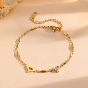 Detalle de una pulsera de acero dorado con dijes de corazón y circonitas transparentes
