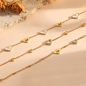 Primer plano de pulseras de corazón en acero titanio dorado con nácar blanco y cristales.