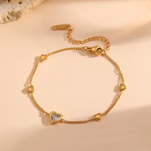 Primer plano de pulsera de acero de titanio chapada en oro con dijes de corazón de cristal.