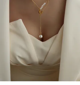 Detail of a 18k gold safety pin Y-necklace with imitation pearl tassel on a female model
