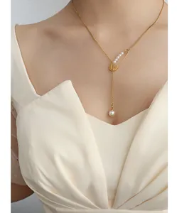 Close-up of 18k gold safety pin pendant necklace with pearls and fringe on a model