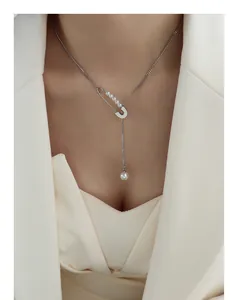 Close-up of safety pin necklace with pearls and fringe pendant on white blazer