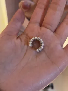 Detail showing a delicate silver ear cuff with white pearls held in a person's hand.