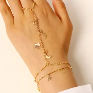 Dettaglio di un bracciale da dito dorato con ciondoli a stella e luna sulla mano