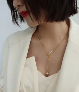 Close-up of gold safety pin necklace with pearls and fringe tassel on a white suit