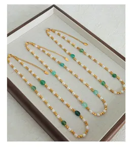 Dettaglio di perle naturali e pietre verdi con perle dorate su un vassoio di lino beige