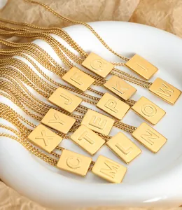 Macro detail of gold square initial pendants on stainless steel chains in a ceramic tray