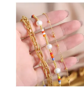 Dettaglio di bracciali a strati con catene dorate, perle d'acqua dolce e perline colorate