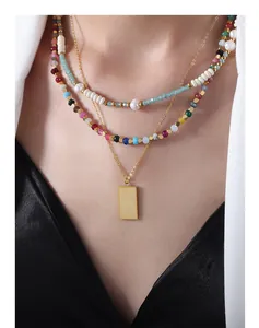 Detalle de collar dorado de varias capas con colgante grabado y cuentas de piedras de colores
