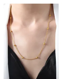 Close-up of a minimalist gold beaded necklace worn by a model in a white suit