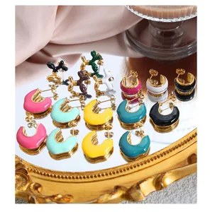 Close-up of balloon dog studs and macaron enamel C-shaped hoop earrings on a mirror