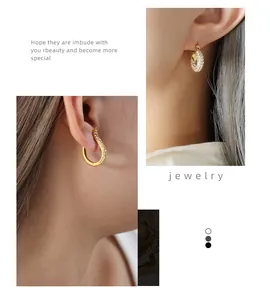 Gros plan de boucles d'oreilles torsadées en U dorées avec zircons blancs sur l'oreille
