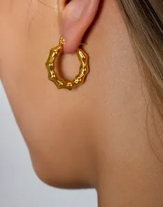 Primer plano de pendientes de aro dorados en forma de C con textura de bambú en modelo