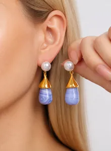 Close-up of gold drop earrings with pearls and purple marbled pendants on a model