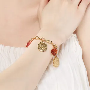 Gros plan d'un bracelet religieux avec médaillons dorés et cœur rouge porté au poignet.