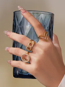 Dreiteiliges goldenes Ring-Set mit Zirkon-Pavé an der Hand vor blauem Glasbecher