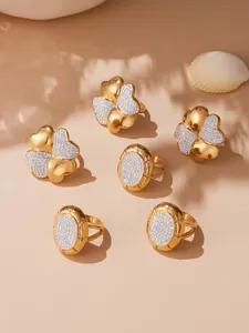 Detail view of 18k gold plated clover rings with white pavé zircons on shell background