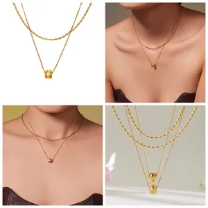 Détail d'un collier doré double couche avec un pendentif cylindrique rayé et des perles