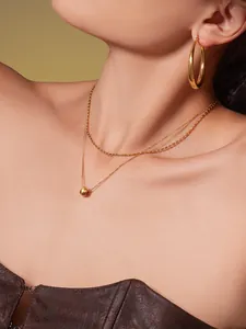 Gros plan du collier double couche doré avec pendentif sphère et créoles sur un modèle