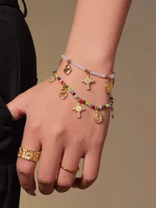Detail von gestapelten rosa Perlenarmbändern mit Herz- und Kreuzanhängern und Goldringen