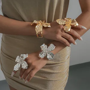 Close-up of metallic wrinkled flower bracelets and rings set on model's hands.