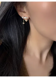 Primo piano di orecchini placcati oro 18k con nappe a fiori e stelle e perle eleganti.
