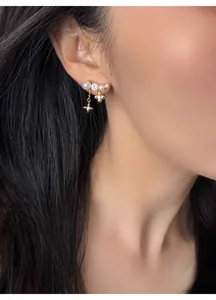Dettaglio orecchini di perle placcati oro 18k con ciondoli a fiore e stella su una modella