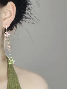 Primo piano di lunghi orecchini a nappa con farfalla in zircone colorato indossati sull'orecchio.