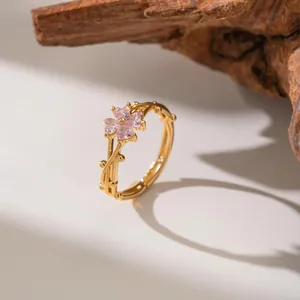 Close-up detail of a gold plum blossom ring with pink crystals and vine design.